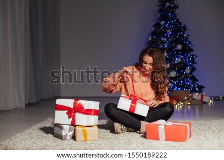 Portrait of a beautiful woman with curls at the Christmas tree with gifts of new year lights garland