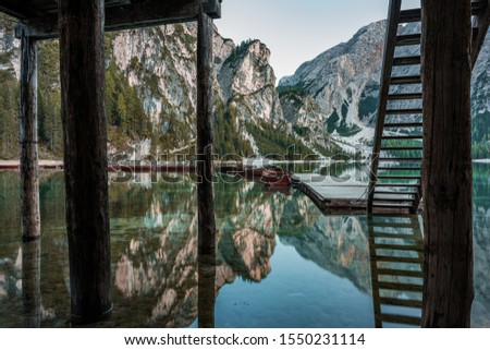 A beautiful scenery of high rocky mountains reflected in Braies lake with wooden stairs near the pier in Italy