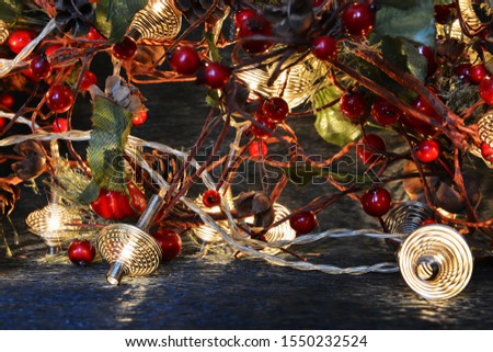 Christmas beautiful greeting card. A spruce twig with red berries and a glowing garland of metal springs on a dark background