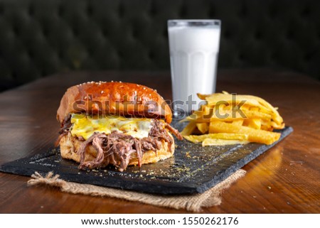 Pulled Beef Hamburger Sandwich Combo Meal with cheddar cheese sauce, Turkish yogurt drink Ayran and fried french fries on wooden table. Copy space for text area.