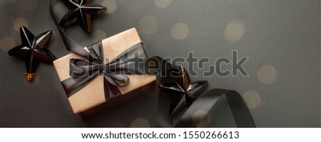 Beautiful minimal christmas golden black decor and paper craft gift box with satin black ribbon on dark black background. Flat lay design. Copy Space. Horizontal, banner
