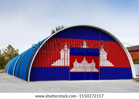 Close-up of the national flag of Cambodia
 painted on the metal wall of a large warehouse the closed territory against blue sky. The concept of storage of goods, entry to a closed area, logistics