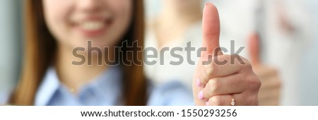 Focus on gorgeous female hand showing big thumb in order to perform approving gesture and greet boss or colleague. Company meeting concept. Blurred background Royalty-Free Stock Photo #1550293256
