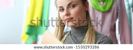 Trendy Clothes Collection Create Industry Concept. Beautiful Blond Seamstress Holding Clipboard with Fashion Sketch. Stunning Woman Looking at Camera. Caucasian Designer at Tailor Shop