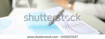 Silver pen lies on paper documents with color business charts background. Statistics financial analysis concept. Development of stock markets and securities strategies