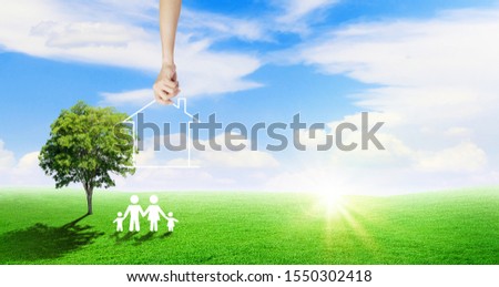 Real Estate and Happy Family Concept : Hand putting house on green grass meadow field nearly family icons and green tree.