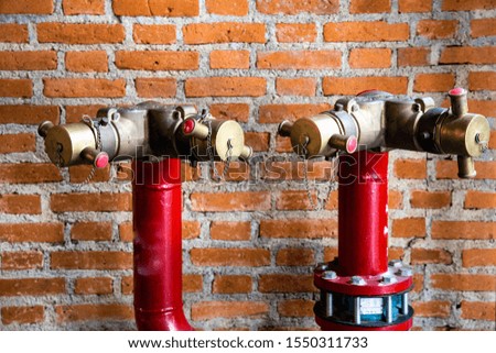 Red metal water pipe of an extinguisher system with brass valves against brown brick wall.