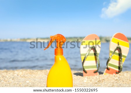 Bottle of sun protection body cream and slippers on beach, space for design