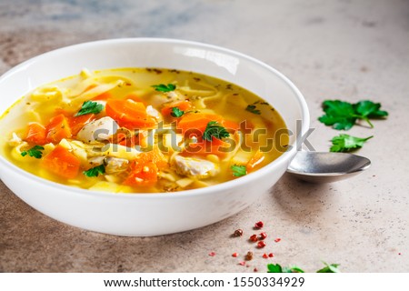 Chicken noodle soup with parsley and vegetables in a white plate, gray background.