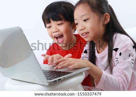 Cute little Asian boy and girl using laptop at home. Siblings using computer isolated on white background.