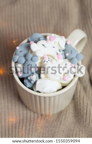 Cocoa with marshmallow in gray and white mouse or rat shape in cup with fairy lights christmas picture. Vertical