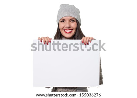 Smiling beautiful young woman in stylish winter fashion holding a blank white sign with copyspace for your text or advertisement