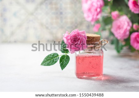 Natural pure rose oil or scented water in bottles for spa, skin care or aromatherapy. Glass bottle on a wooden table, small pink roses with leaves. Organic cosmetics concept. Selective focus