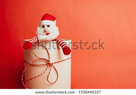 a toy Santa sticking out of a gift box on a red background. The concept of Christmas and a happy new year. Space for your text
