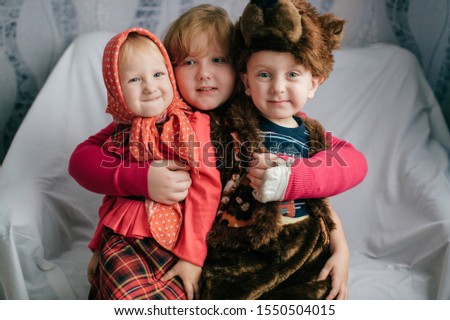 Portrait of beautiful girl hugs her little brother in bear costume and funny young sister in russian style festive dress.  Happy childhood.
