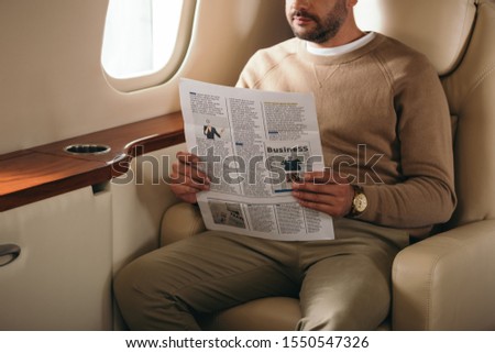 cropped view of bearded man holding newspaper in private jet 