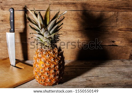 Pineapple with hard shadow. Against the background of an old wooden board. Cutting board and knife. Healthy food concept.