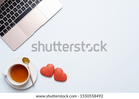 Valentine's Day composition. Female desktop with laptop, ?up of tea and ginger cookie as heart on pastel background. Valentine day concept, flat lay design. Top view