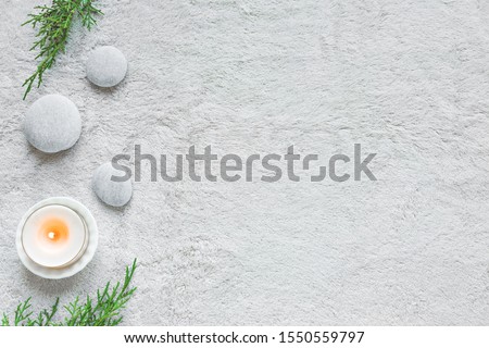 Spa concept on white soft towel background, green leaves, candle and zen like stones, top view, copy space.