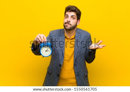 young handsome man with an alarm clock against orange background