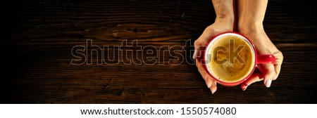 Dark mood wooden desk of free space for your text or product.Woman hands holding cup of coffee in cafe interio. Dark mood photo with shadows and flat lay. Copy space. Aerial view. Winter time. 