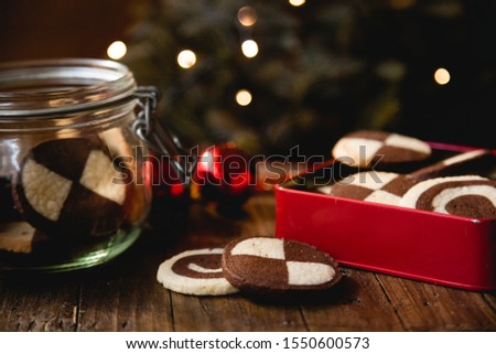 Traditional German Christmas cookies (checkered biscuits) in red biscuit tin on wooden table with christmas decoration and lights in the background