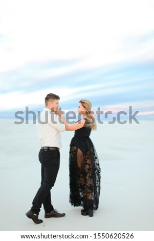 Young blonde woman wearing transparent black dress walking with man in snowed field.