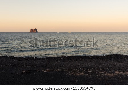 The small promontory of Strombolicchio from Stromboli's black beach at sunset in Sicily, Italy.