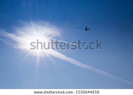 Blue sky . Against the background of blue sky and bright sun, an airplane is flying. Basic background for design.Aircraft flying in the sky against a background of a bright sunset.