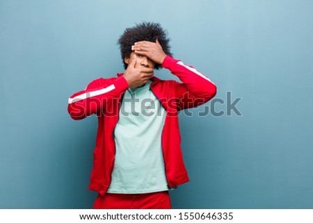 young black sports man covering face with both hands saying no to the camera! refusing pictures or forbidding photos against grunge wall