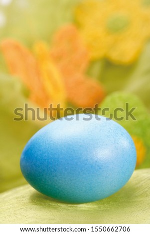 Pastel-coloured Easter egg in a nest with out-of-focus butterfly decoration in background