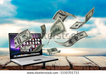 Finance and earning concept, one hundred dollar banknotes flying around laptop, internet, side view on dark background.