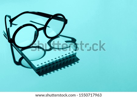 black round glasses lie on a Notepad and cast a shadow on the mint background