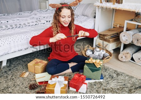 Charming smiling young woman taking photos of Christmas gifts and sharing on social media