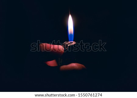 ็Hand holding a  lighter with a large flame in darkness.