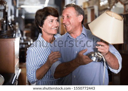 positive mature couple is shopping the old lamp for home in the antique store