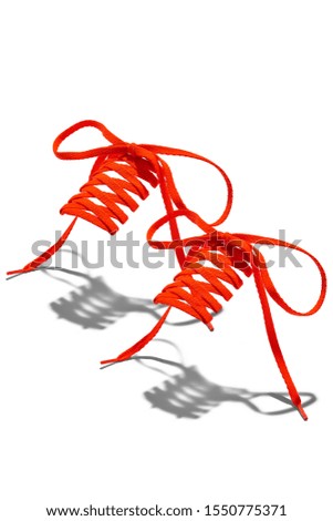 The photo of bright orange wicker shoelaces with bright orange tips, hanging in the air on a white background. Shoelaces is casting a shadow. 