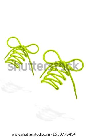 The photo of light green wicker round shoelaces with light green tips, hanging in the air on a white background. Shoelaces is casting a shadow. 