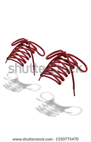 The photo of red and black wicker round shoelaces with red tips, hanging in the air on a white background. Shoelaces is casting a shadow. 