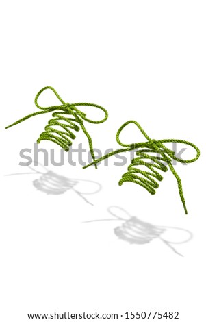 The photo of bright green and grey wicker round shoelaces with bright green tips, hanging in the air on a white background. Shoelaces is casting a shadow. 