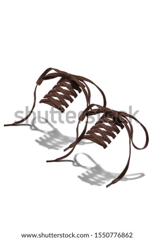 The photo of brown wicker shoelaces with brown tips, hanging in the air on a white background. Shoelaces is casting a shadow. 