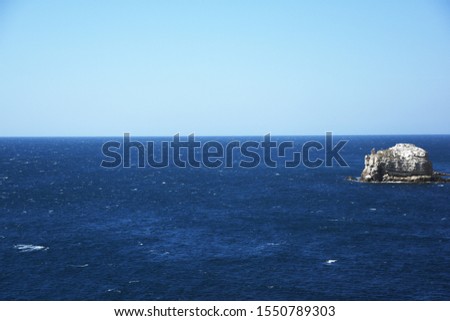 The horizon of the connection of the blue sky and the blue boundless sea. A rock sticks out of the water to the right. The sea is calm and calm, the beauty of nature.