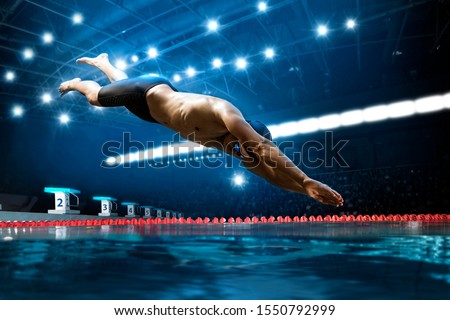 Professional young muscular swimmer jumping from starting block in a swimming pool Royalty-Free Stock Photo #1550792999