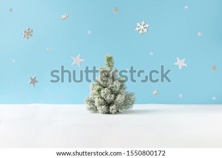 Creative layout with snowy Christmas tree, stars and snowflakes on bright blue background. Minimal winter nature holiday scene.