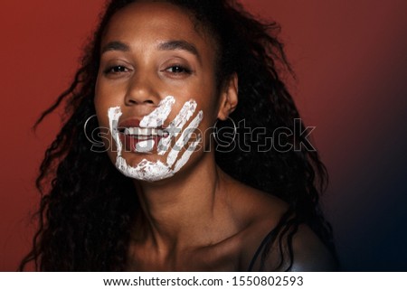 Close up of a smiling young african woman with white hand print on her face isolated over red background