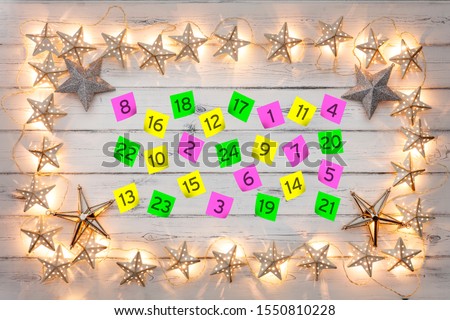 Advent calander parer notes, with a border of golden star christmas lights, on a distressed white wooden board