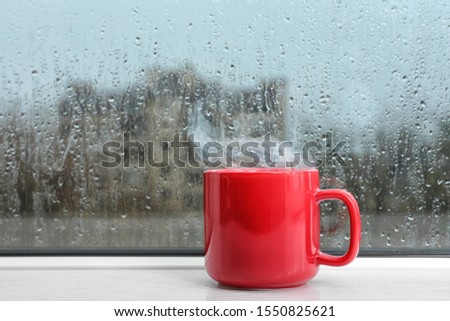 Cup of hot drink on white windowsill. Rainy weather