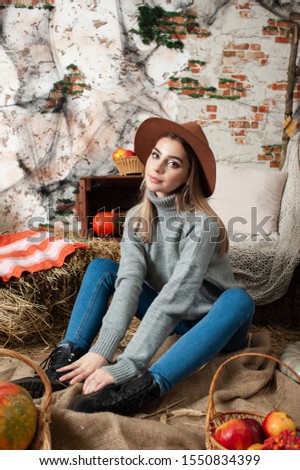 girl sitting in a sweater, hat and jeans among the hay, pumpkins (Halloween theme)
