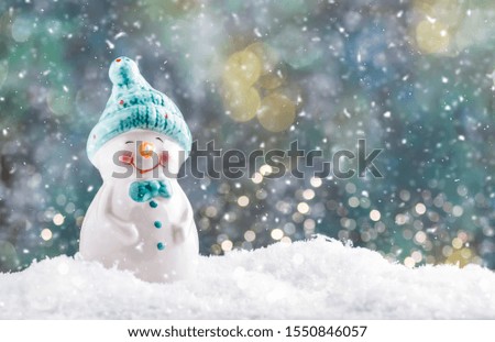 Porcelain snowman figurine in snowdrift, Christmas or New Year background with snowflakes and lights
