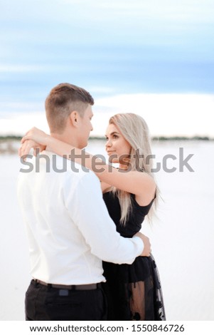 Young caucasian woman wearing black transparent dress hugging man in snow field background. Concept of love and winter photo session.